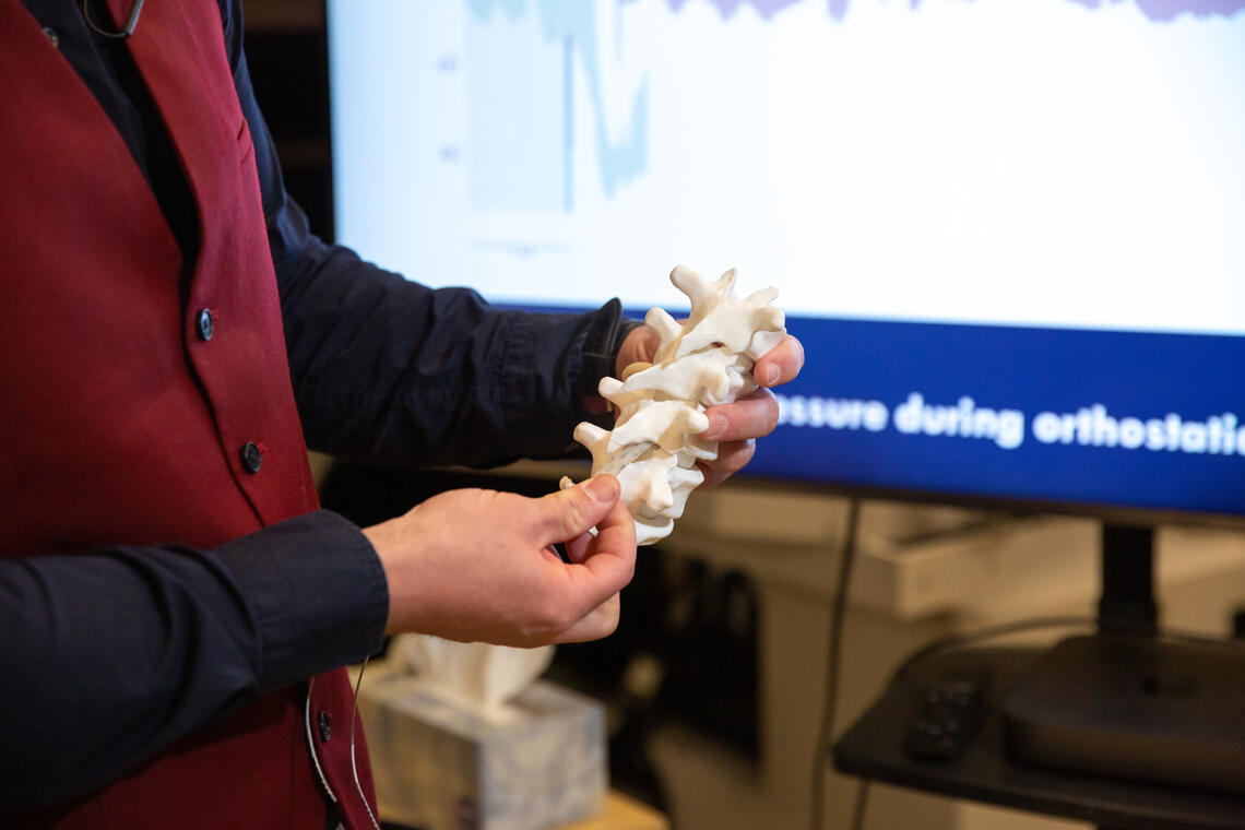 Aaron Phillips, PhD, uses a model of a spine to demonstrate where the stimulator will be placed.