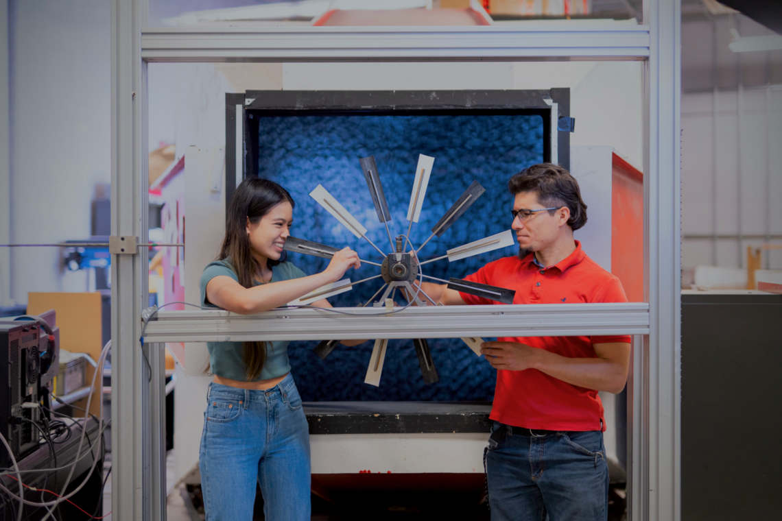 A student and a mentor work together on a mechanical piece of equipment in a lab.