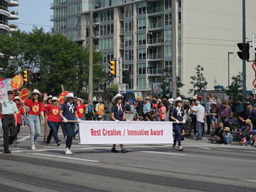 People walking with a banner ahead of the UCalgary's new float. The banner reads "UCalgary's new float"