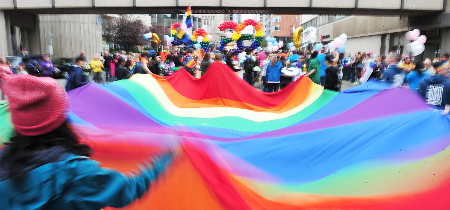 UCalgary parade walkers carrying the LGBTQ+ flag