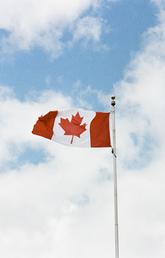 A Canadian flag flies proudly against a partly-cloudy sky