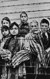 A black and white image depicting a group of children behind a barbed wire fence dressed in striped prison clothes at the Auschwitz concentration camp
