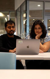 A group of students crowd around one laptop