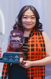 A woman wears a checkered scarf and smiles at the camera holding an award