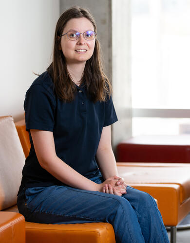 SSHRC Storytellers finalist Jennifer Williamson in a black shirt and jeans sitting on an orange sofa