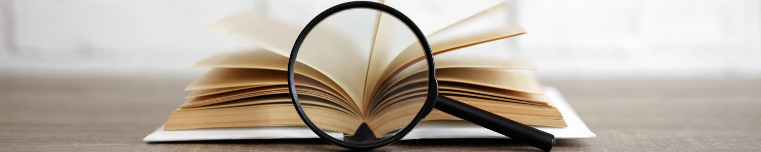 A book open on a table with a magnifying glass in front of the book.