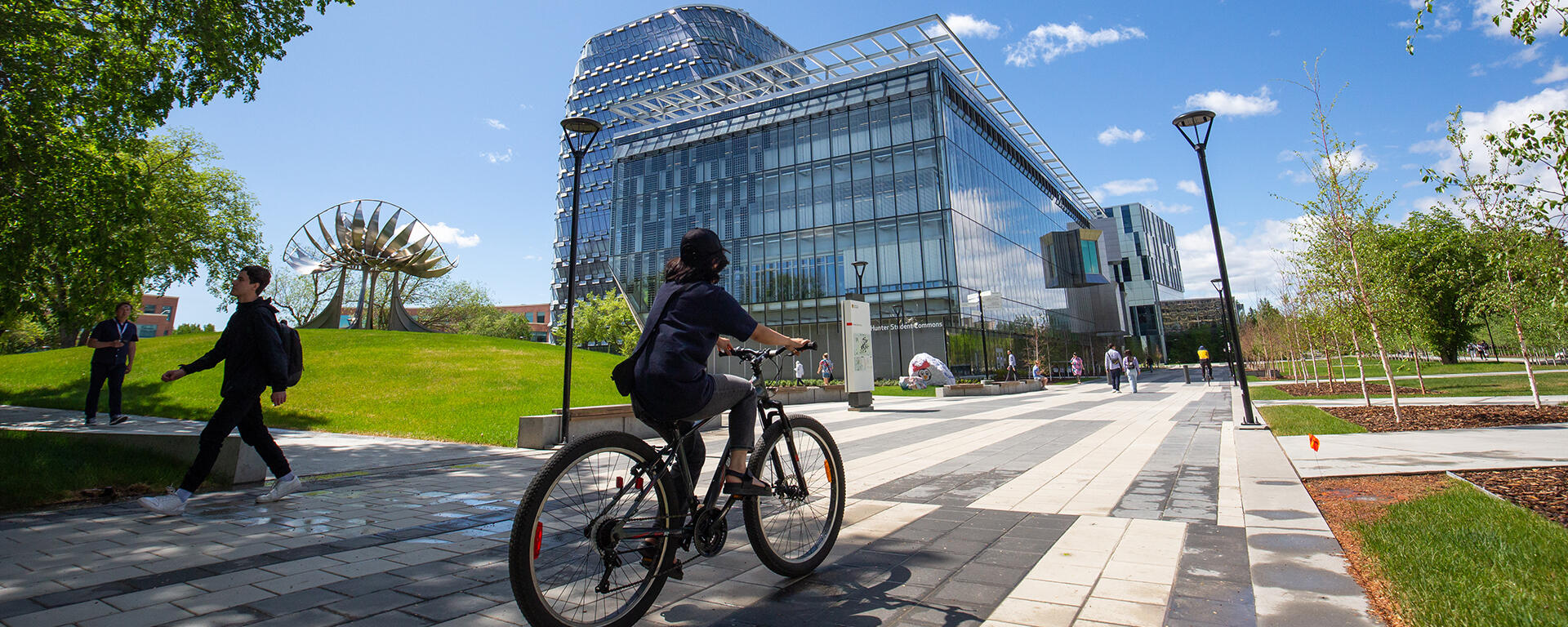 Cyclist riding in front of the Hunter Hub and MacKimmie Tower on sunny day.