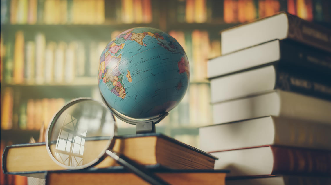 globe and magnifying glass on stack of books