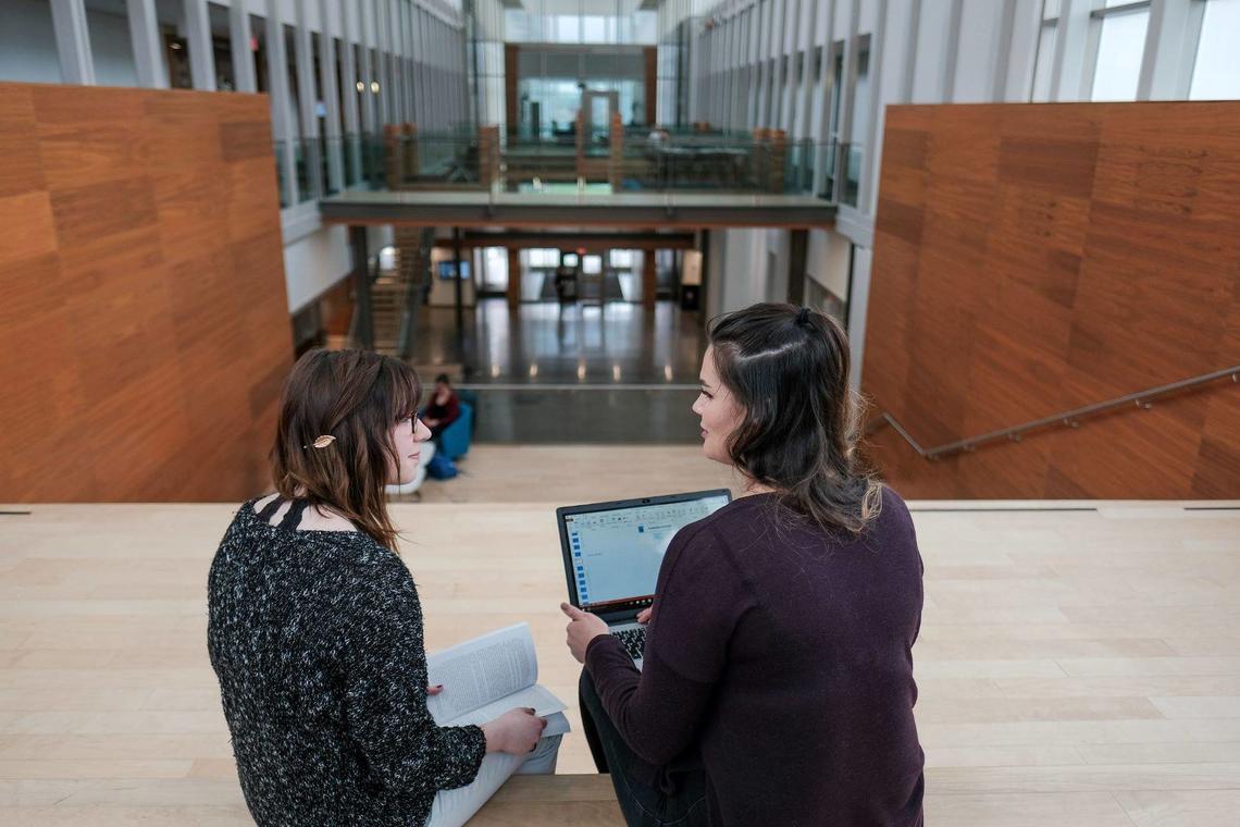 Virtual Micro-Pod Tutoring Two students talking with an open book and laptop